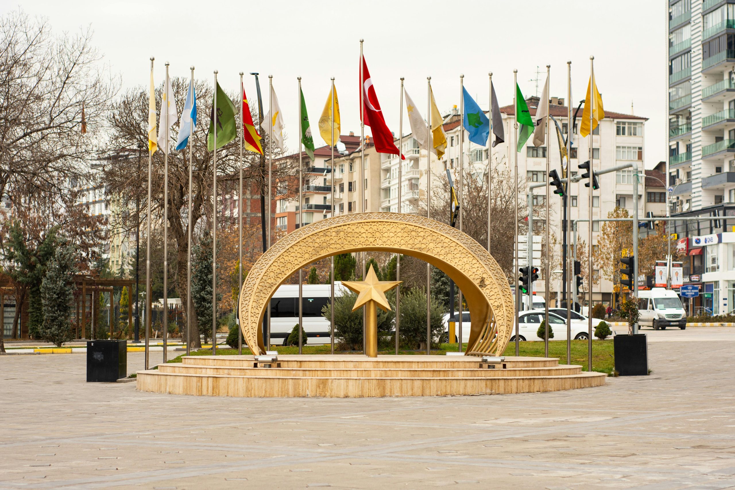 Golden crescent and star sculpture surrounded by international flags in city square.